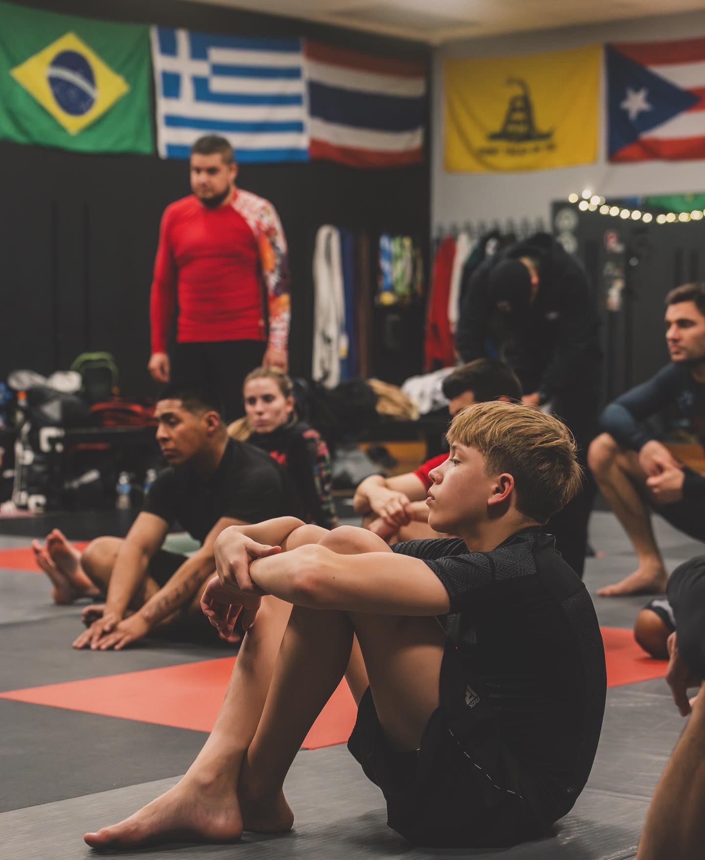 Students of all ages sitting along the mats listening during a class at the academy