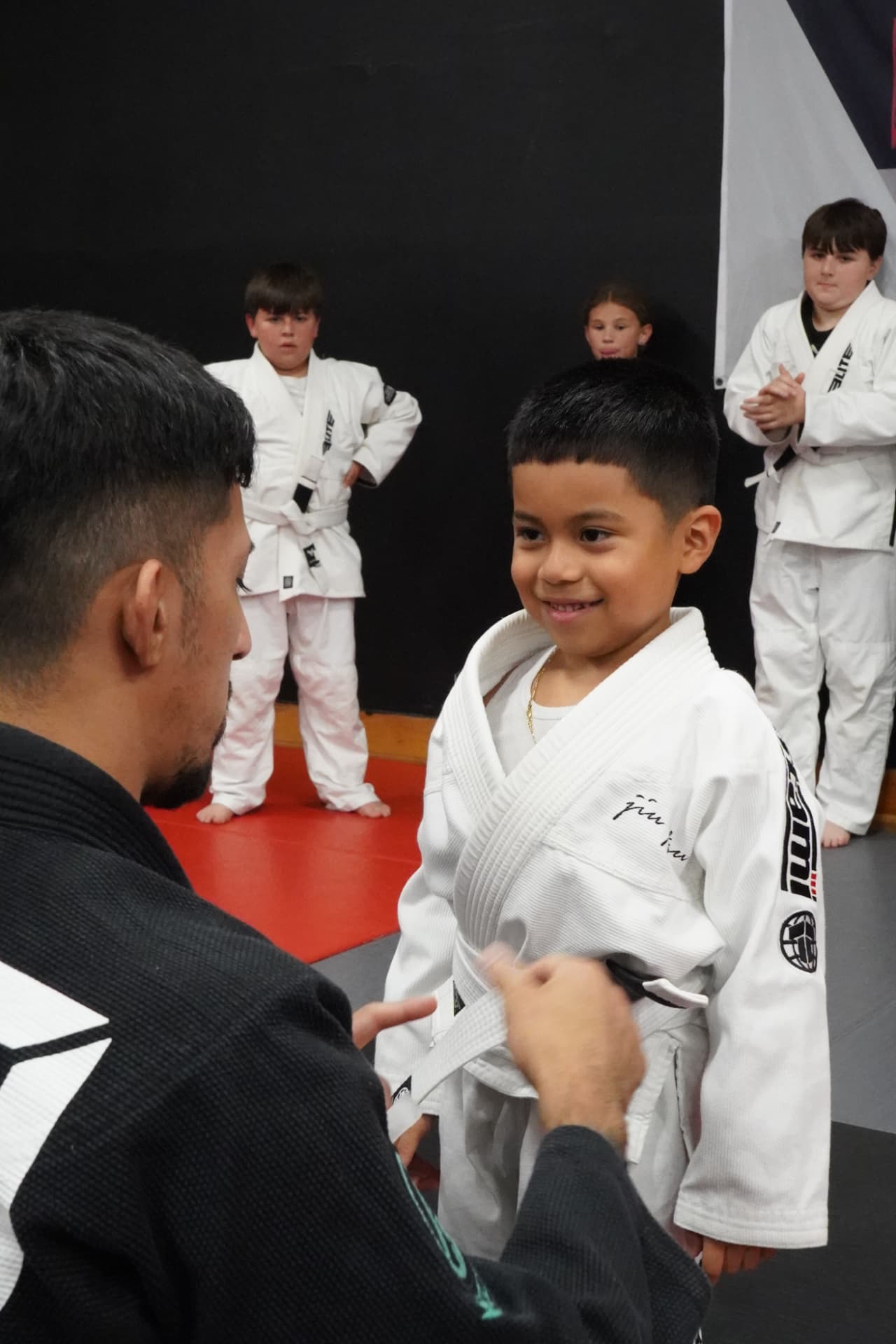 Coach adjusting a young student's belt during a kids jiu-jitsu class