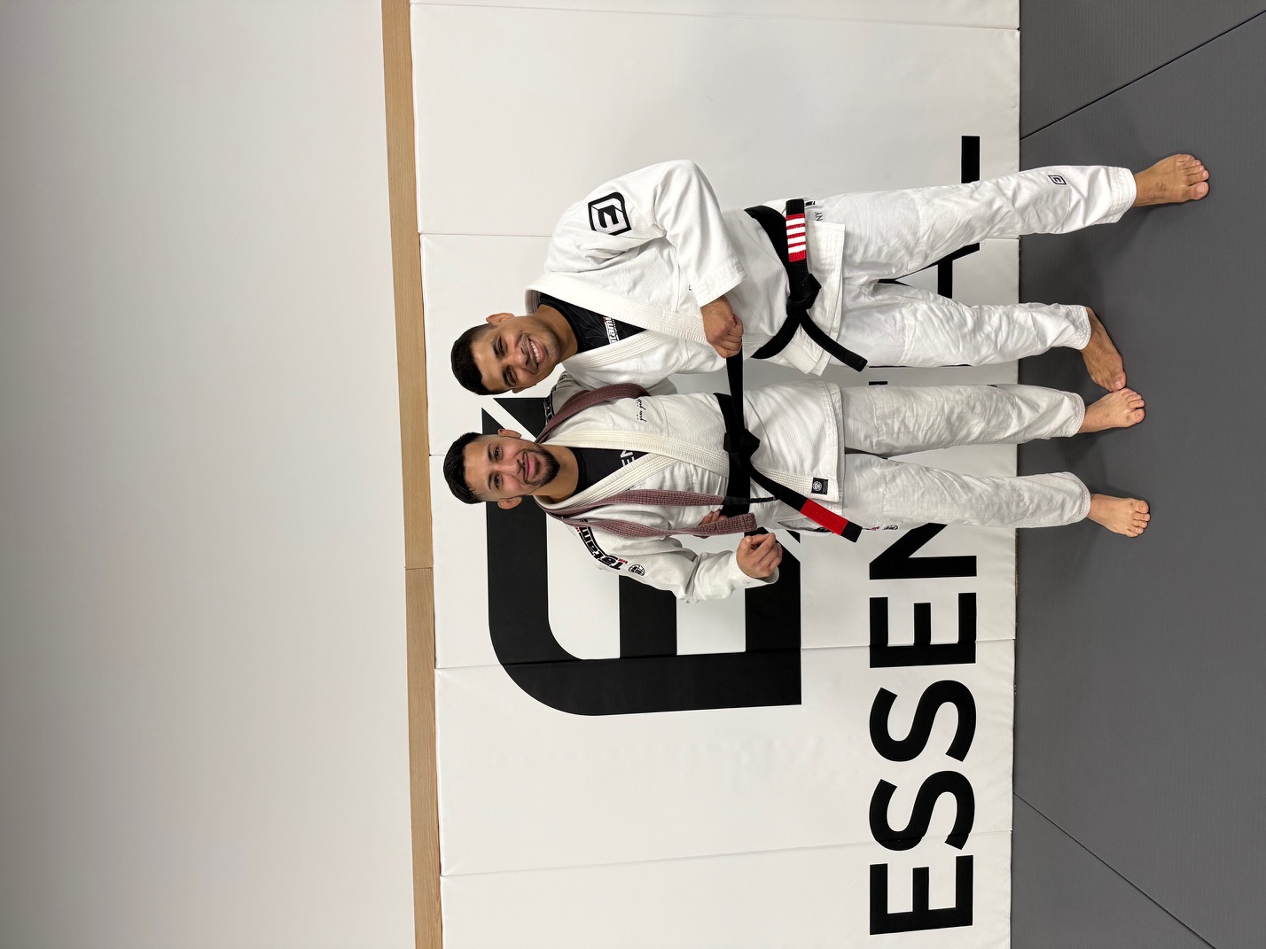 Two Pressure black belts in white gis standing together on the academy mats